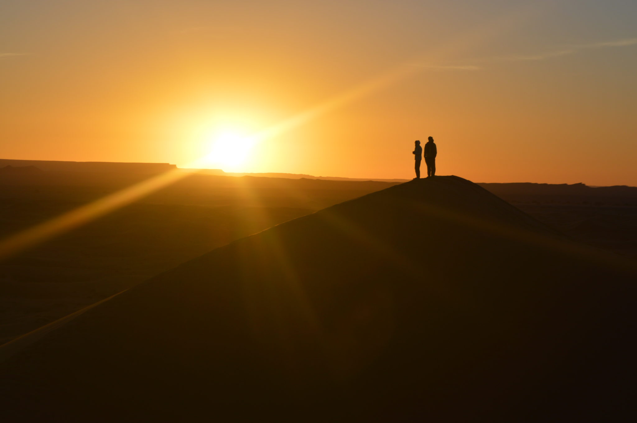 Three distant figures stand and watch the sunrise in the Sahara