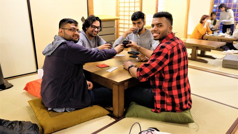 Four friends drinking sake and sitting on tatami mat