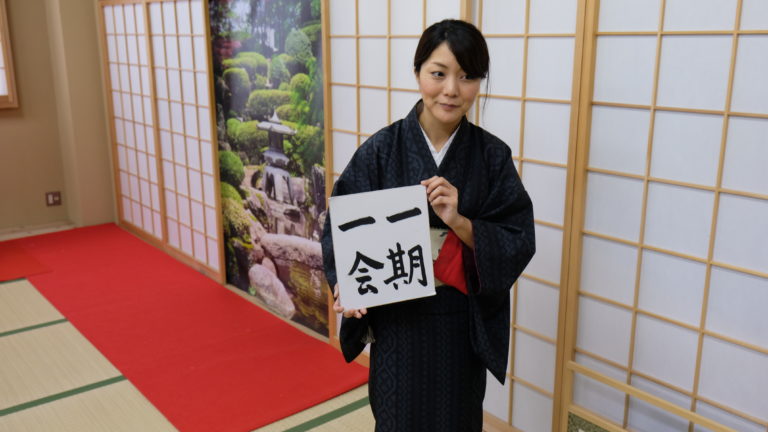 Tea Master holds up a poster with the Japanese characters for Ichi Go Ichi e