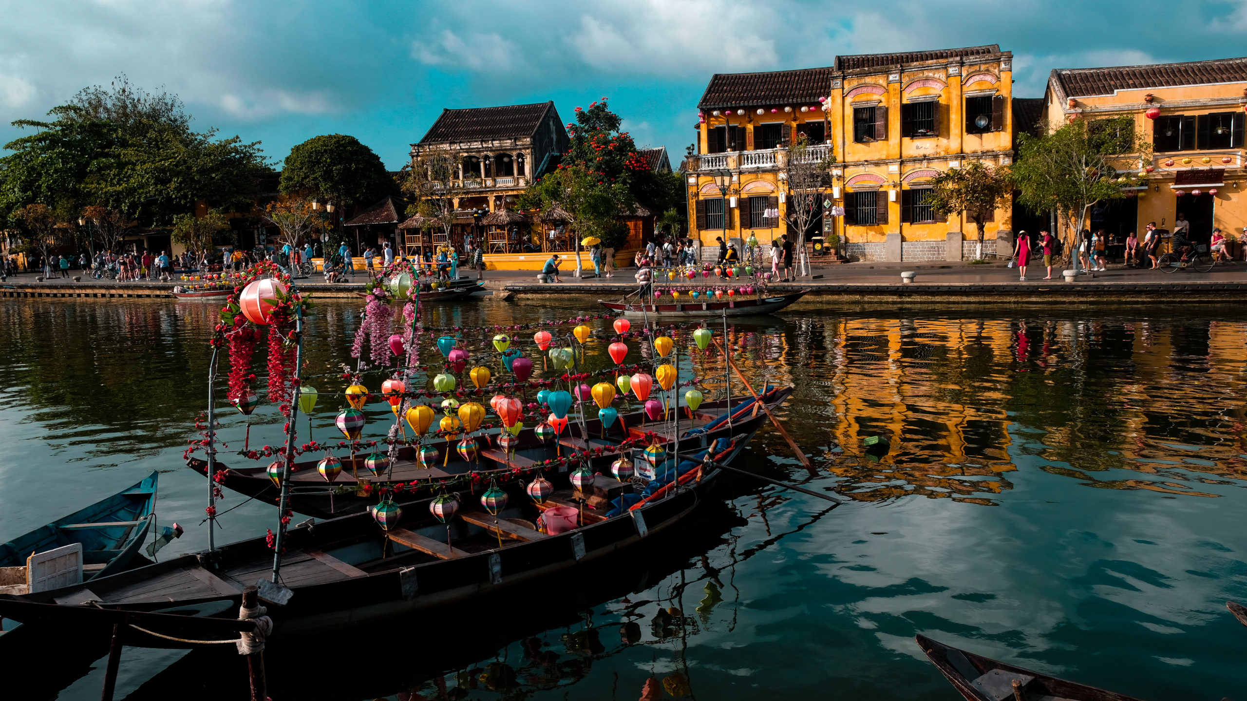 A boat with lanterns sits facing a yellow house in Hoi An