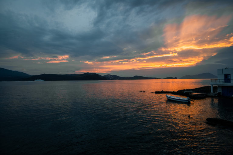 Sun sets as sea darkens and boat sits in the water